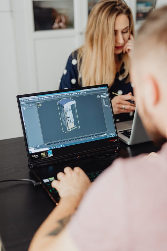 a-man-using-laptop-5904083 Two colleagues working on laptops indoors, focusing on 3D modeling software.
